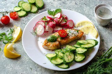 Salmon steak with lemon, tomatoes, cucumber and radish on a plate. Healthy seafood. Proper nutrition food.
