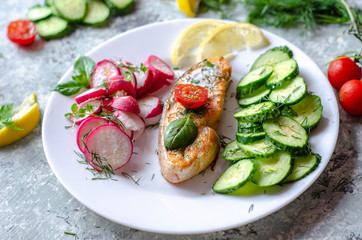 Salmon steak with lemon, tomatoes, cucumber and radish on a plate. Healthy seafood. Proper nutrition food.