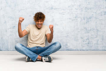 Young african american man sitting on the floor celebrating a victory