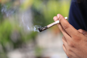 Man hand holding smokes a marijuana cannabis joint on green background, Medical marijuana should not be used in illegal ways.