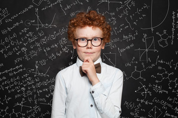 Thinking child boy student on blackboard background with science formulas