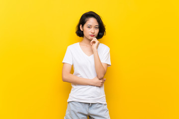 Asian young woman over isolated yellow wall thinking