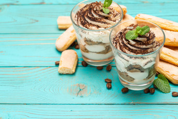 Classic tiramisu dessert in a glass and savoiardi cookies on blue wooden background