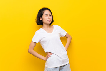 Asian young woman over isolated yellow wall suffering from backache for having made an effort