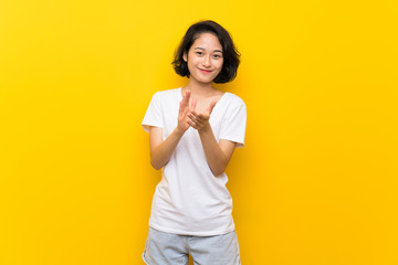Asian young woman over isolated yellow wall applauding after presentation in a conference