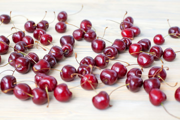 A lot of red berries of sweet cherry scattered on light wooden table close up, bunch of ripe cherry berries on white blurred background macro, heap of cherries top view, fresh natural summer dessert