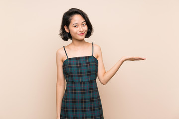 Asian young woman over isolated yellow wall holding copyspace imaginary on the palm to insert an ad