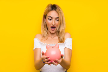 Obraz na płótnie Canvas Young blonde woman over isolated yellow wall holding a big piggybank