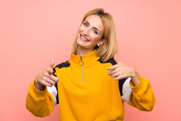 Young blonde woman over isolated pink background pointing to the front and smiling