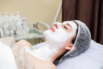 Obraz na płótnie Canvas Face mask, spa beauty treatment. Young beautiful girl applying facial clay mask at spa salon, skin care concept.