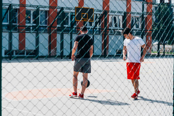 Two strong basketball player playing ball on an urban city basketball court, while wearing black and red outfit.