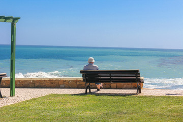 Naklejka na ściany i meble Man sitting on bench overlooking sea, Praia da Luz Beach, Lagos, Algarve, Portugal