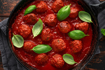 Homemade Meatballs in iron cast with sweet and hot tomato sauce, basil. On wooden table