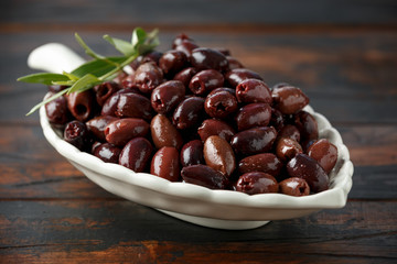 Pitted kalamata olives in bowl on rustic wooden background