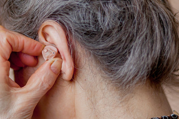 closeup senior woman inserting hearing aid in her ears