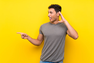 Handsome man over isolated yellow wall surprised and pointing finger to the side