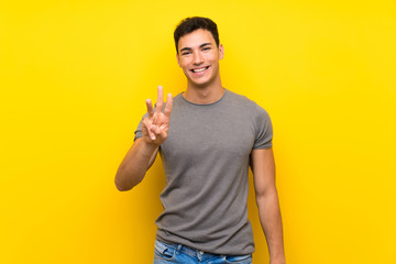 Handsome man over isolated yellow wall happy and counting three with fingers