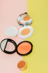 Make up products spilling on to a bright yellow and pink background with copy space