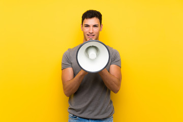 Handsome man over isolated yellow wall shouting through a megaphone