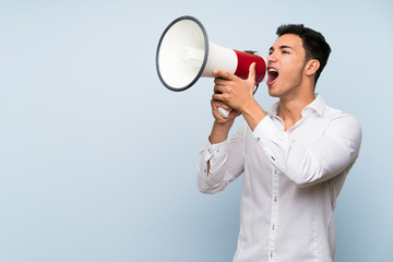 Handsome man over blue wall shouting through a megaphone
