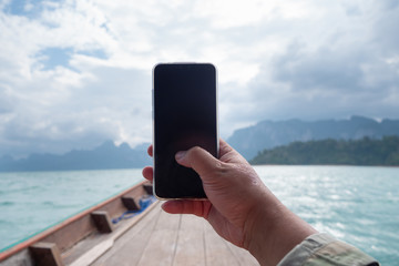 Hand of man using mobile smart phone against scenic landscape of boat view in the big river and reservoir dam with mountain and nature forest
