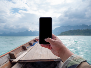 Hand of man using mobile smart phone against scenic landscape of boat view in the big river and reservoir dam with mountain and nature forest
