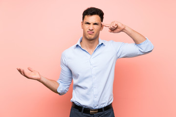 Handsome man over pink background making the gesture of madness putting finger on the head