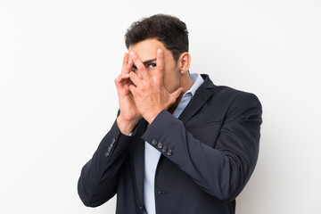 Handsome man over isolated white wall covering eyes and looking through fingers