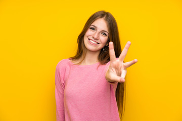 Young woman with long hair over isolated yellow wall happy and counting three with fingers