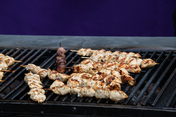 Large open outdoor barbecue grill cooking kabobs made of chunks of chicken on wooden skewers.