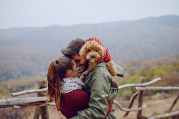 Cute couple in love standing in nature and cuddling. Man holding dog on shoulders. Autumn season.