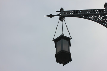 Street lantern black and white image on gloomy day. Lantern hanging on old vintage pole outdoors 