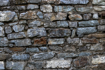 The old stone wall is lined with stone of various shades of gray and brown. Background.