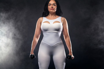 Size plus woman sporty fit woman in white sportswear, athlete with dumbbells makes fitness...