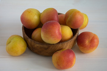 Top view of apricots in wooden bowl on white wooden background