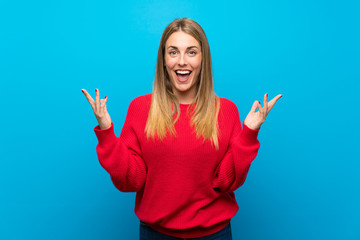 Woman with red sweater over blue wall smiling a lot