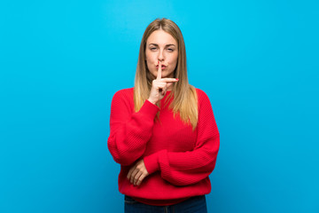 Woman with red sweater over blue wall showing a sign of silence gesture putting finger in mouth