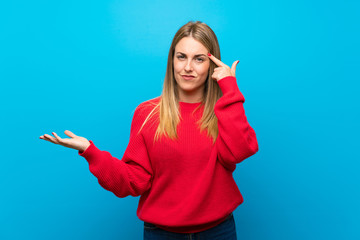 Woman with red sweater over blue wall making the gesture of madness putting finger on the head