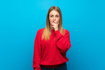 Woman with red sweater over blue wall surprised and shocked while looking right