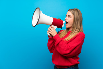 Woman with red sweater over blue wall shouting through a megaphone