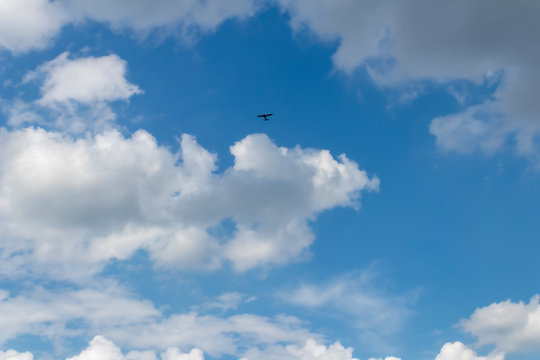 Single engine airplane flying in a cloud filled blue sky
