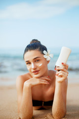 Suntan lotion woman applying sunscreen solar cream. Beautiful happy cute woman  applying suntan cream from a plastic container to her nose with ocean in background.