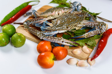 Raw crab on wooden plate with lemon, basil, pepper, tomato and garlic at white background, Sea food.