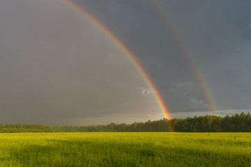 Beautiful landscape with dramatic sky and double rainbow. Green field under cloudy sky with double rainbow.