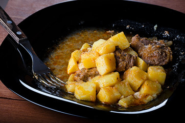 braised potatoes with meat and gravy on a black plate, closeup 45 view