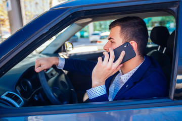 Businessman talking on his phone while driving his city car in the traffic jam.