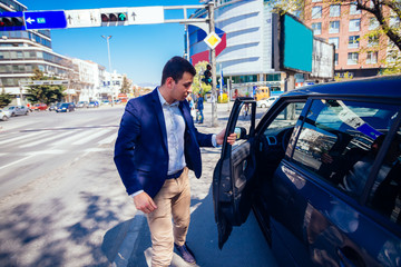 Fototapeta premium Happy entrepreneur opening his car door and inspecting the interior of his car while being parked next to a busy city boulevard.