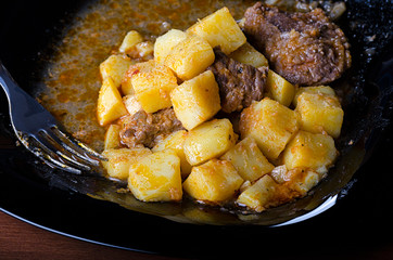 braised potatoes with meat and gravy on a black plate, closeup 45 view