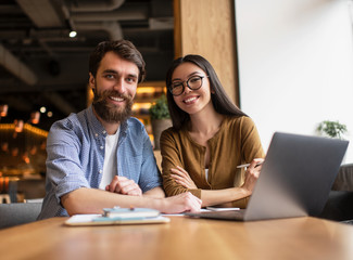 Business colleagues sitting at table in office, using laptop computer, working together for startup project. Successful business and career concept. Portrait of young happy developers at workplace