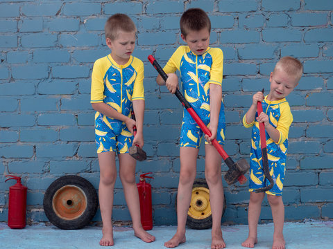Funny children in swimsuits for boys posing in front of camera on background of brick wall. Brothers dream of adventure, travel, exploits. Children hold hammers and sledge hammer